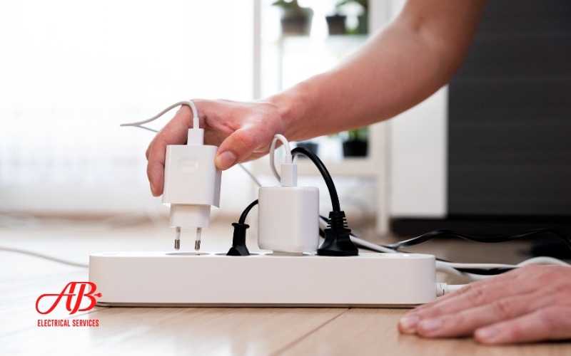 AB Electrical Services Person plugging a white charger into a power strip on a wooden floor. Orange County CA