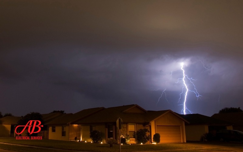 AB Electrical Services A residential neighborhood at night with a visible lightning bolt in the cloudy sky. A logo in the bottom left corner reads, "AB Electrical Services. Orange County CA
