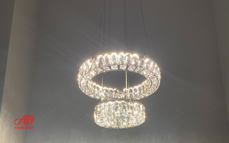 AB Electrical Services A dual-ring crystal chandelier is lit against a gray ceiling. Orange County CA