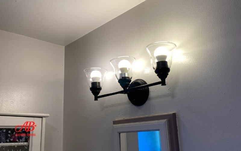 AB Electrical Services A three-bulb wall sconce with glass shades is mounted on a white wall above a doorway. Orange County CA