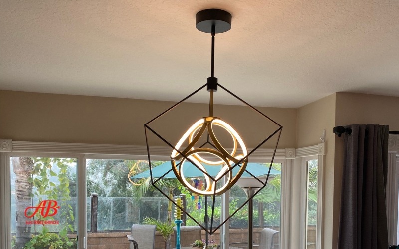 AB Electrical Services A modern geometric chandelier featuring circular LED lights serves as the perfect lighting fixture in a room with large windows, offering a stunning view of the balcony and lush greenery. Ideal for enhancing any home environment with its sleek design. Orange County CA