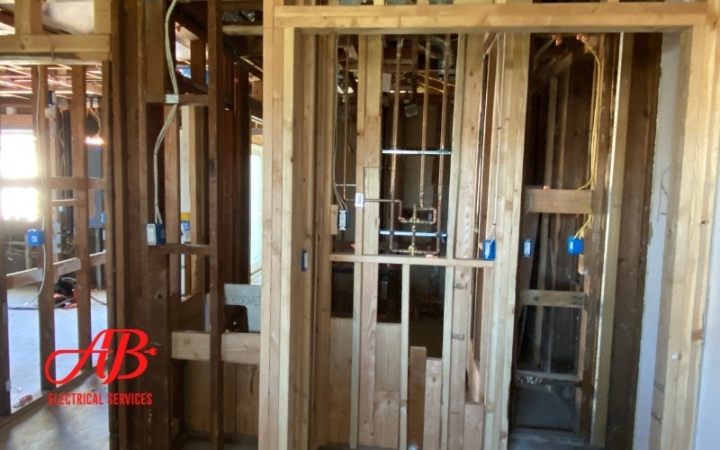 AB Electrical Services Amidst the wooden framework of a building under construction, exposed electrical wiring and plumbing are visible. A logo in the corner reads "AB Electrical Services," highlighting key signs that it might be time to rewire your home for safety. Orange County CA