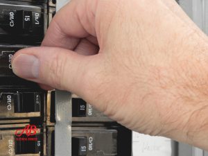 AB Electrical Services A hand flips a switch on an electrical circuit breaker panel, addressing breakers tripping issues. A business logo reading "AB Electrical Services" is visible in the bottom left corner. Orange County CA