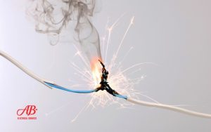 AB Electrical Services Two electrical wires sparking and burning at the point of contact, emitting smoke and sparks, with the AB Electrical Services logo in the lower left corner—highlighting the urgent need for an emergency electrician. Orange County CA