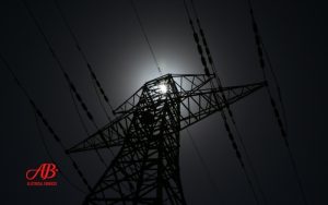 AB Electrical Services Silhouette of an electrical transmission tower with power lines against a dark sky, the sun partially visible behind the structure—highlighting the importance of having the right size backup generator for your home. "AB Electrical Services" logo is in the lower left corner. Orange County CA