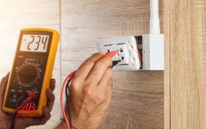 AB Electrical Services A person uses a digital multimeter to measure voltage at a wall electrical outlet, displaying a reading of 234 volts—essential for effective electrical troubleshooting. Orange County CA
