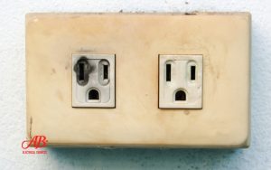 AB Electrical Services A beige electrical outlet with two sockets; the left socket appears burnt and damaged—an urgent electrical sign of possible trouble, while the right socket looks intact. Orange County CA